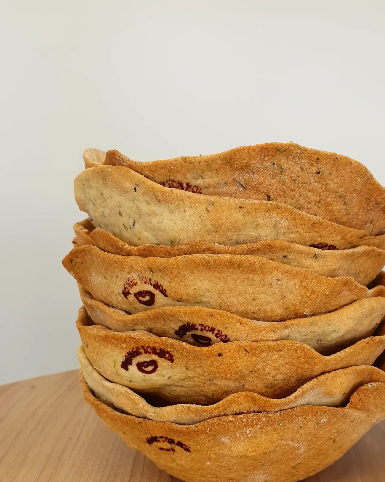 Pile de bols comestibles Mange ton Bol en pâte à pain aux herbes, marqués du logo, posés sur une table en bois